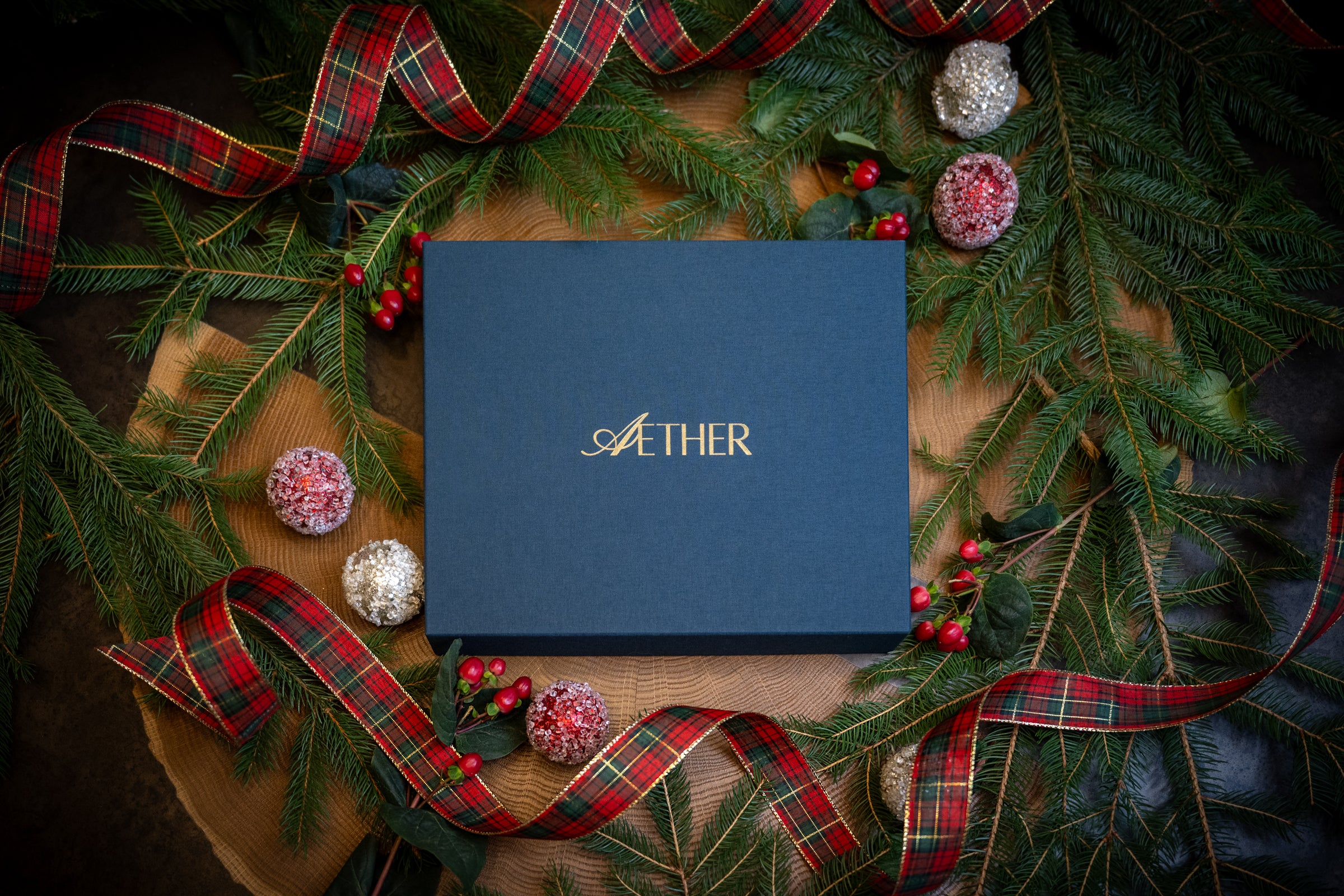 Blue linen Aether box  stamped with a gold foil label, surrounded by festive holiday greenery and ribbons