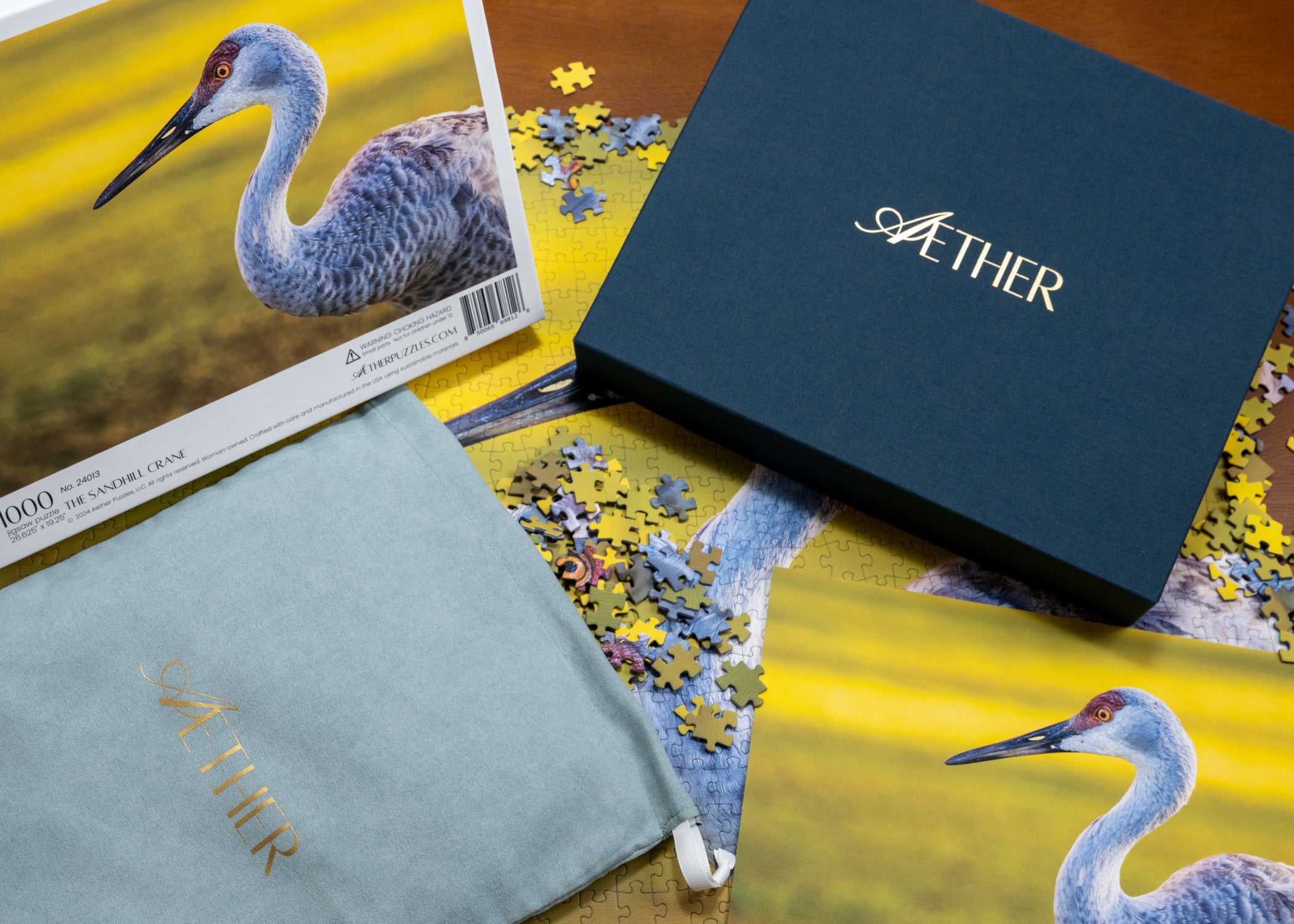 Sandhill crane puzzle, linen gold foil stamped Aether puzzle box, and a sueded velvet puzzle bag on a wooden surface.